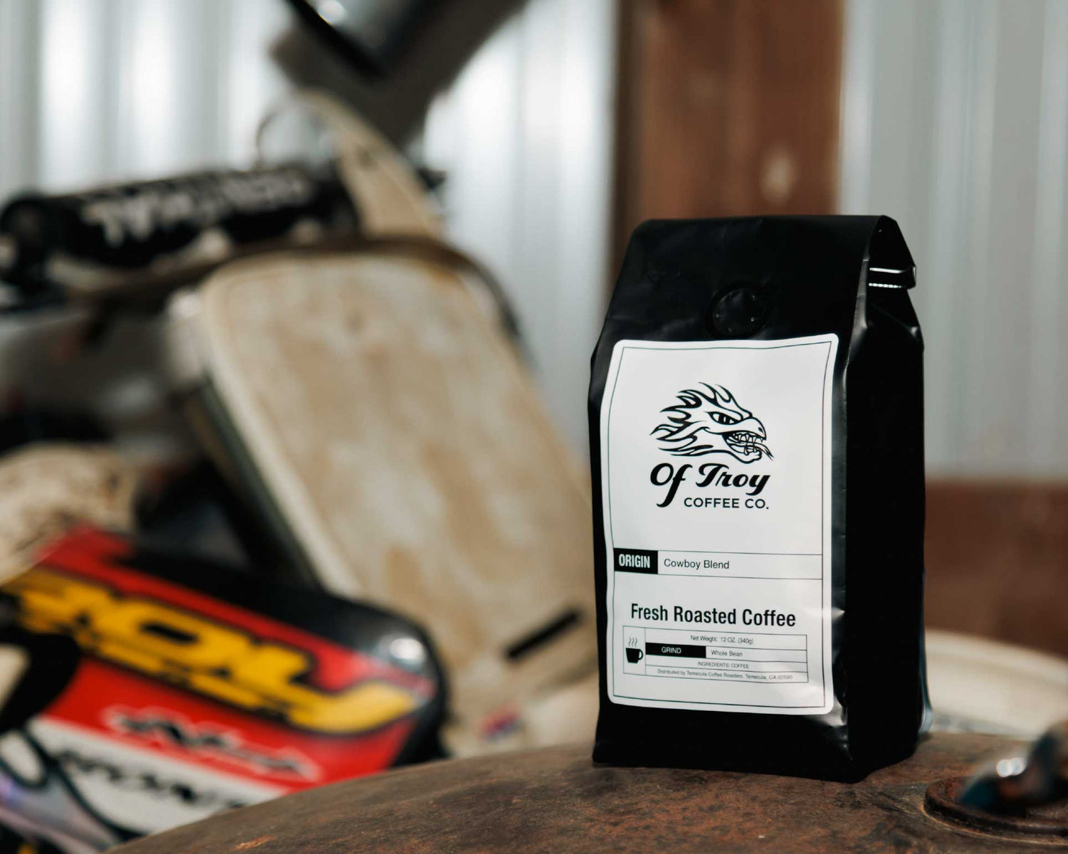Coffee bag from Of Troy Coffee Co. on a motorcycle seat with a blurred background